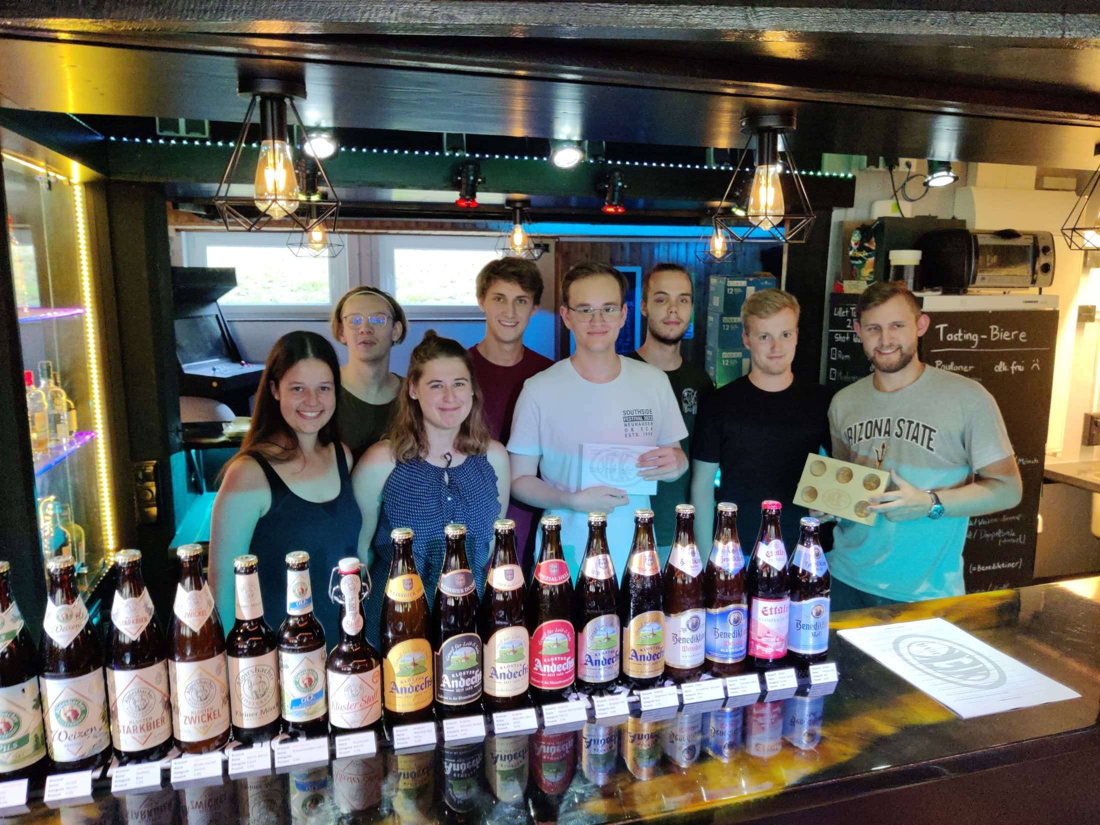 Biertasting-Veranstaltung in der Hauseigenen Bar. Einige Menschen posieren vor vielen Flaschen in einer Bar