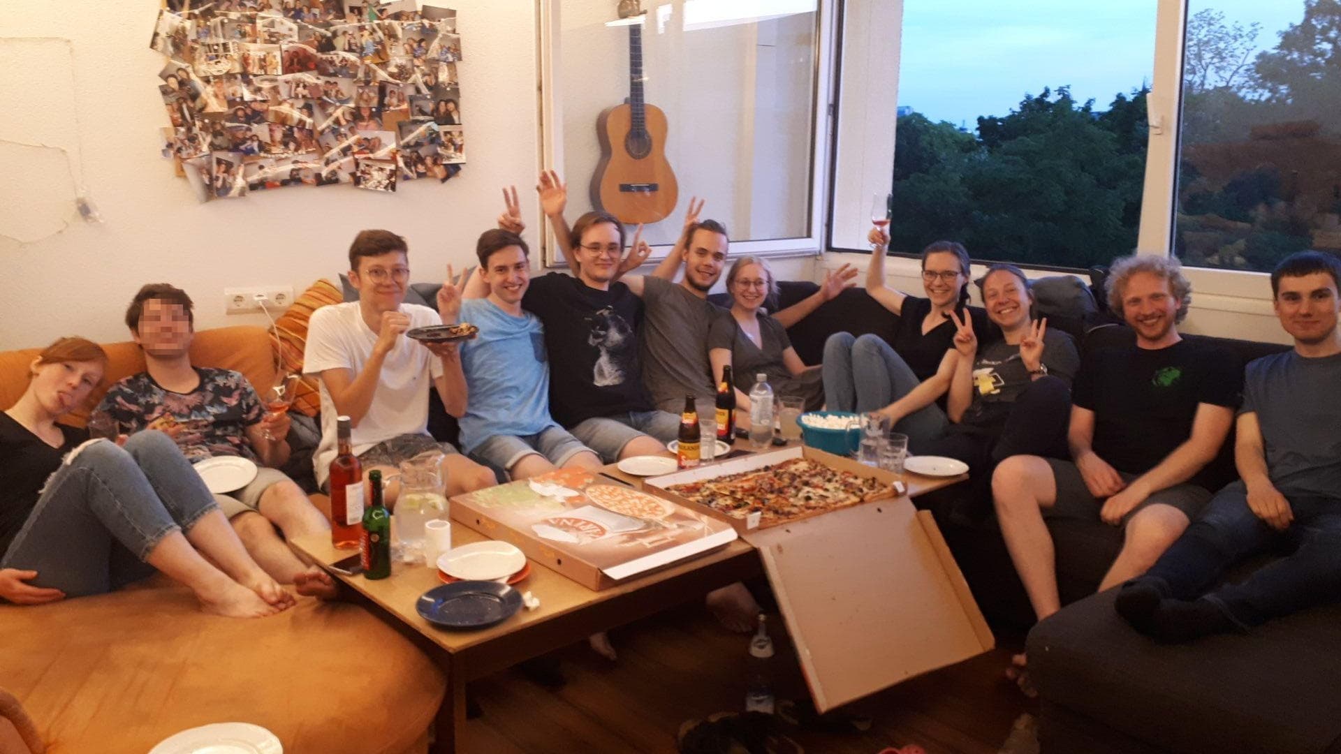 Gemeinsames Pizzaessen und ESC gucken im Etagenraum. Einige Menschen sitzen auf einem Sofa und essen Pizza