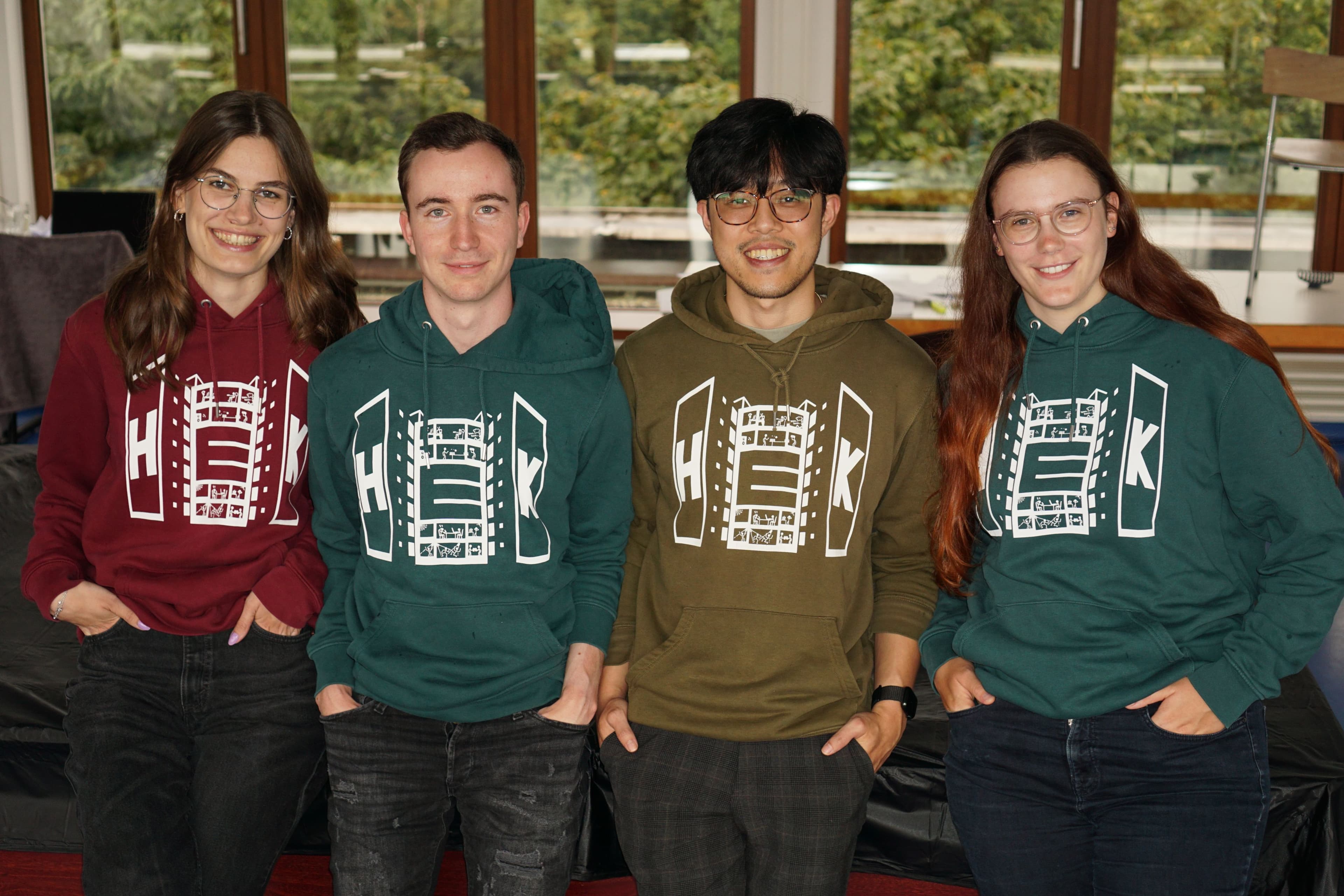 Die Mitglieder der HSV auf einer Bank vor dem HEK. Vier Menschen mit roten Hoodies posieren auf einer Bank im Grünen