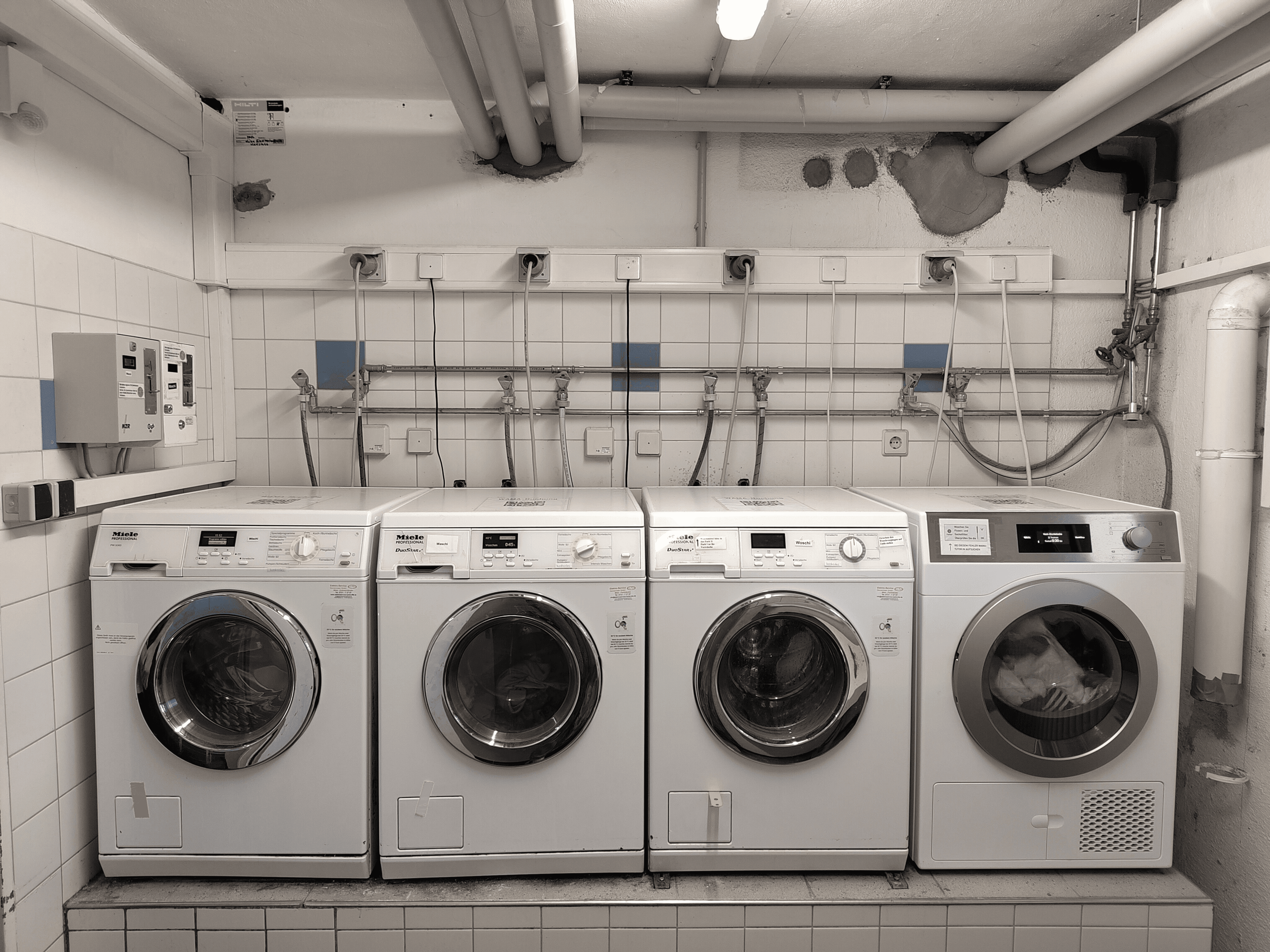 Drei Waschmaschinen und ein Trockner stehen nebeneinander in einem Waschkeller